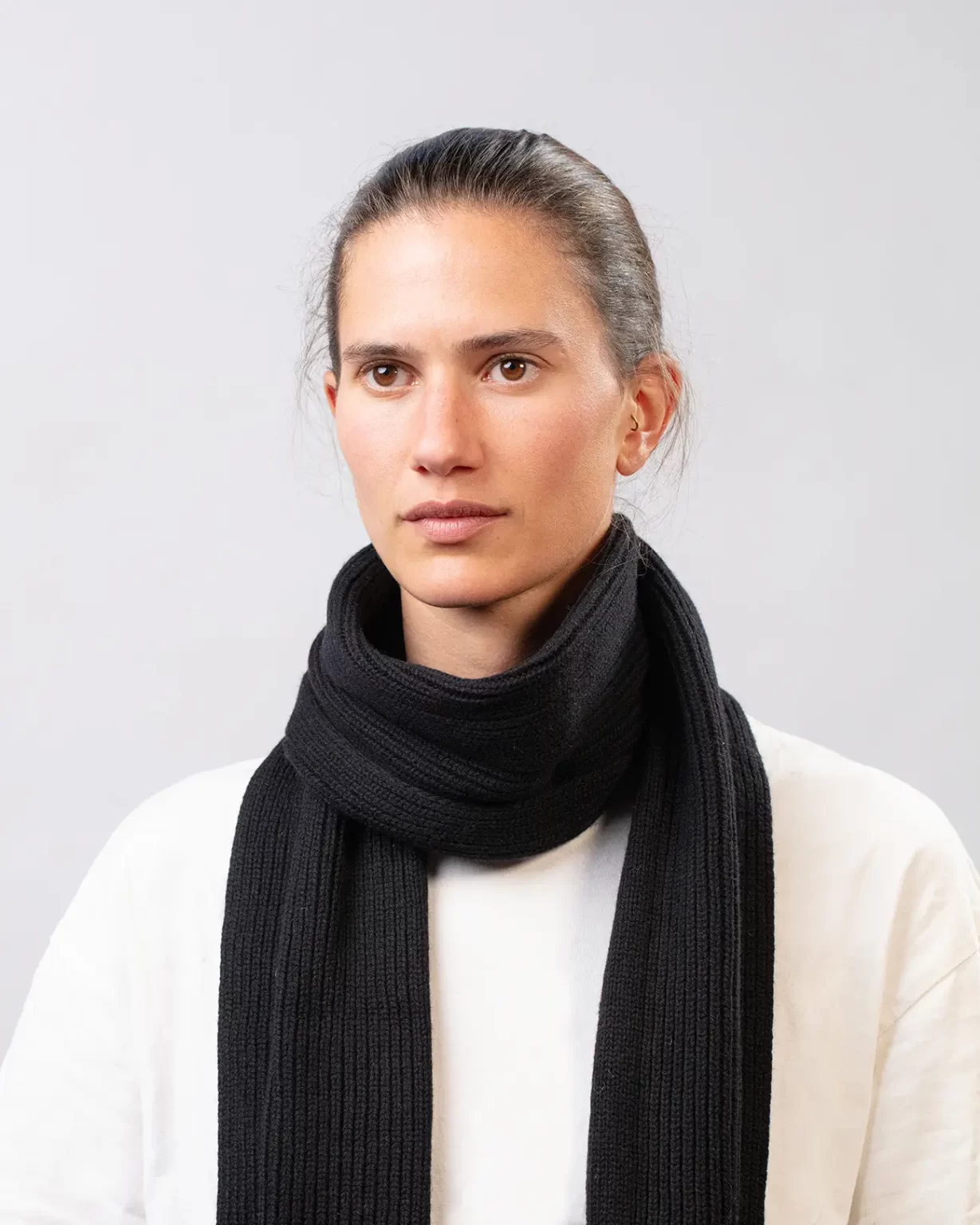 Photographie studio de l'Echarpe Cachemire Régénéré Noir, porté par un mannequin Femme. Cette écharpe est fabriqué en France, à partir de Laine et de Cachemire Recyclé, par la marque haut-de-gamme Maison Douillet. Cest un modèle pour Homme et Femme.