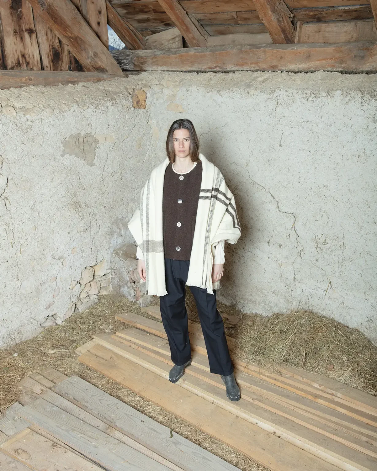 Photo d'une tenue de prêt à porter de la marque Maison Douillet, portée par un modèle femme. Le mannequin porte le Gilet d'Alpage Unisex, couleur marron, la Couverture d'Alpage, et le Pantalon en Laine - tous ces vêtements sont unisex.