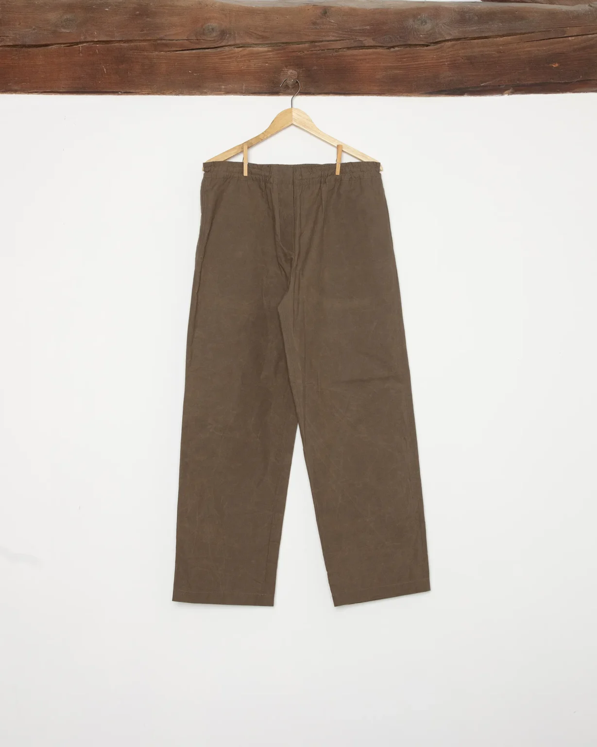 Pantalon marron de la marque Maison Douillet pour homme et femme en coton déperlant biologique. Photo produit prise en studio avec élément de décors en bois rappelant les Alpes.