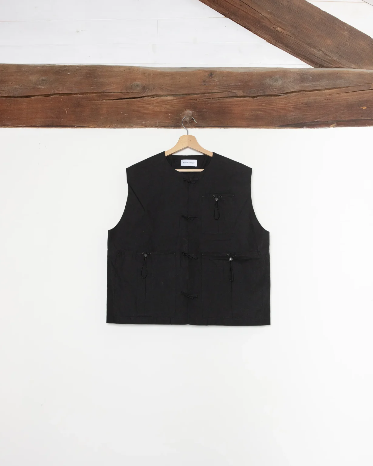 Gilet sans manche noir de la marque Maison Douillet pour homme et femme en coton déperlant biologique. Photo produit prise en studio avec élément de décors en bois rappelant les Alpes.